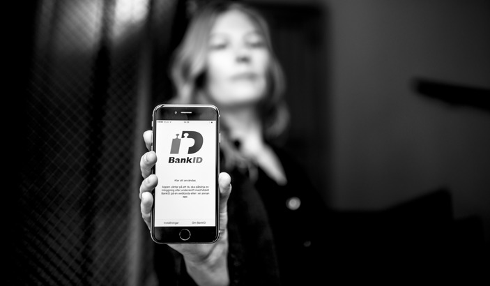 Hand som håller fram en mobiltelefon som visar en vy av BankID-appen.
